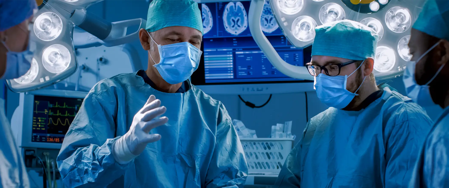 Three surgeons in blue scrubs conversing with each other in a clinical setting.