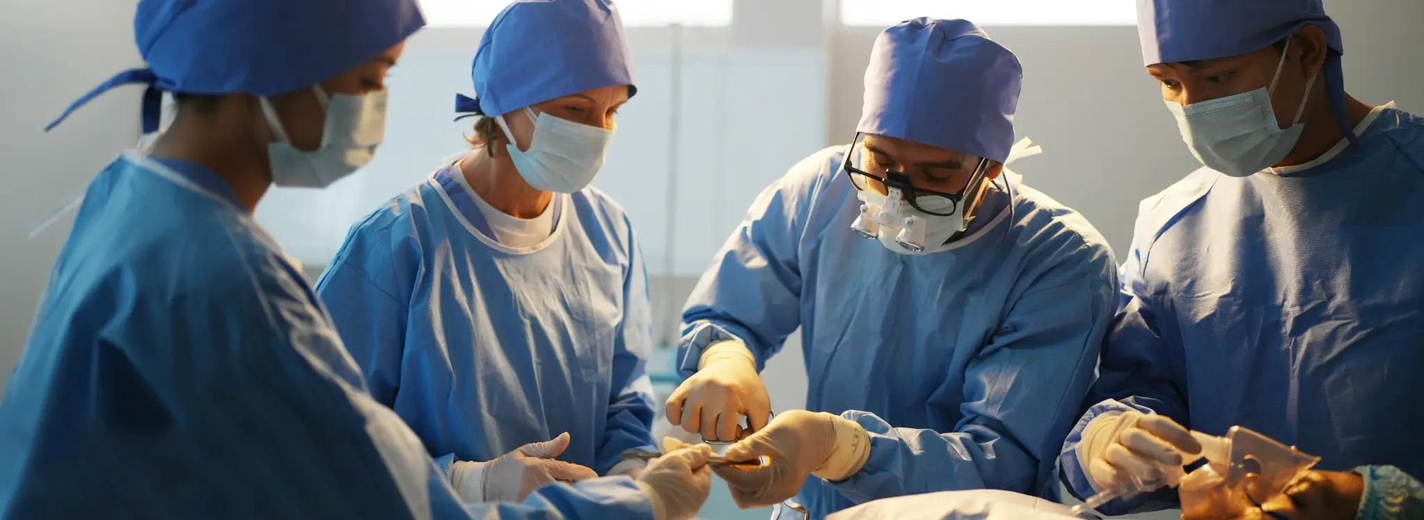 A surgical team in blue scrubs performing a procedure under a bright operating room light